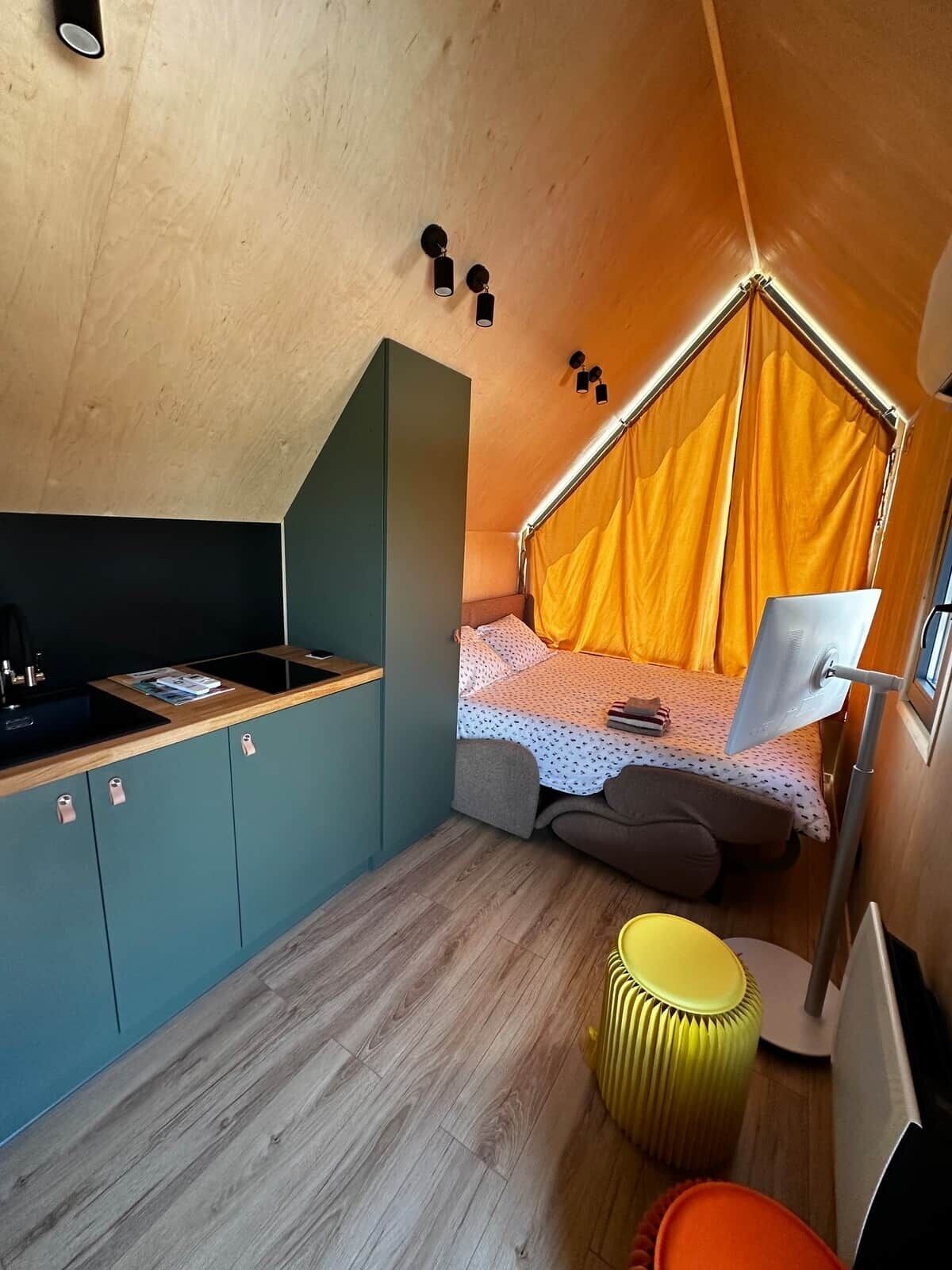 Een compacte kamer met kitchenette, een bed met hemel en een klein zithoekje.