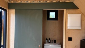A compact, modern bathroom with a wooden ceiling, a small window, and a white sink.