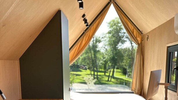 A compact room with a bed, a small kitchen area, and a window with a view of greenery.