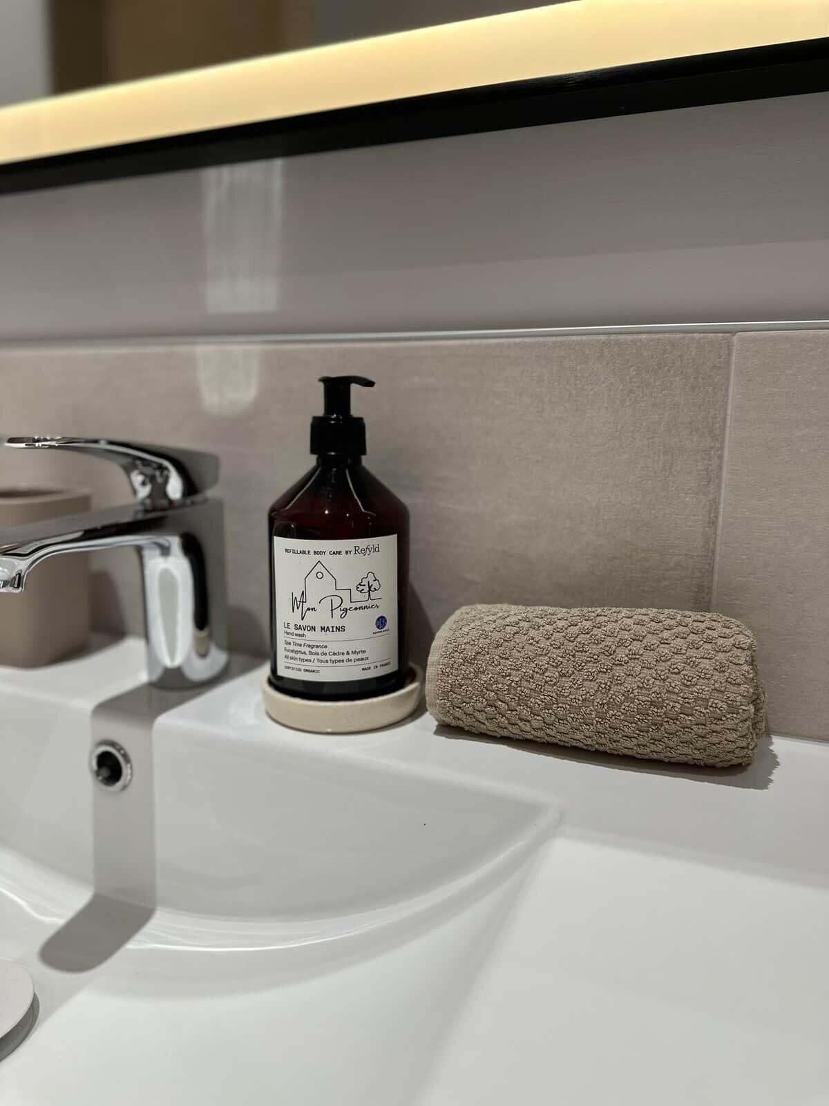 Ein Badezimmer mit einem weißen Waschbecken, einer Handseifenflasche und einem beige gefärbten Handtuch.