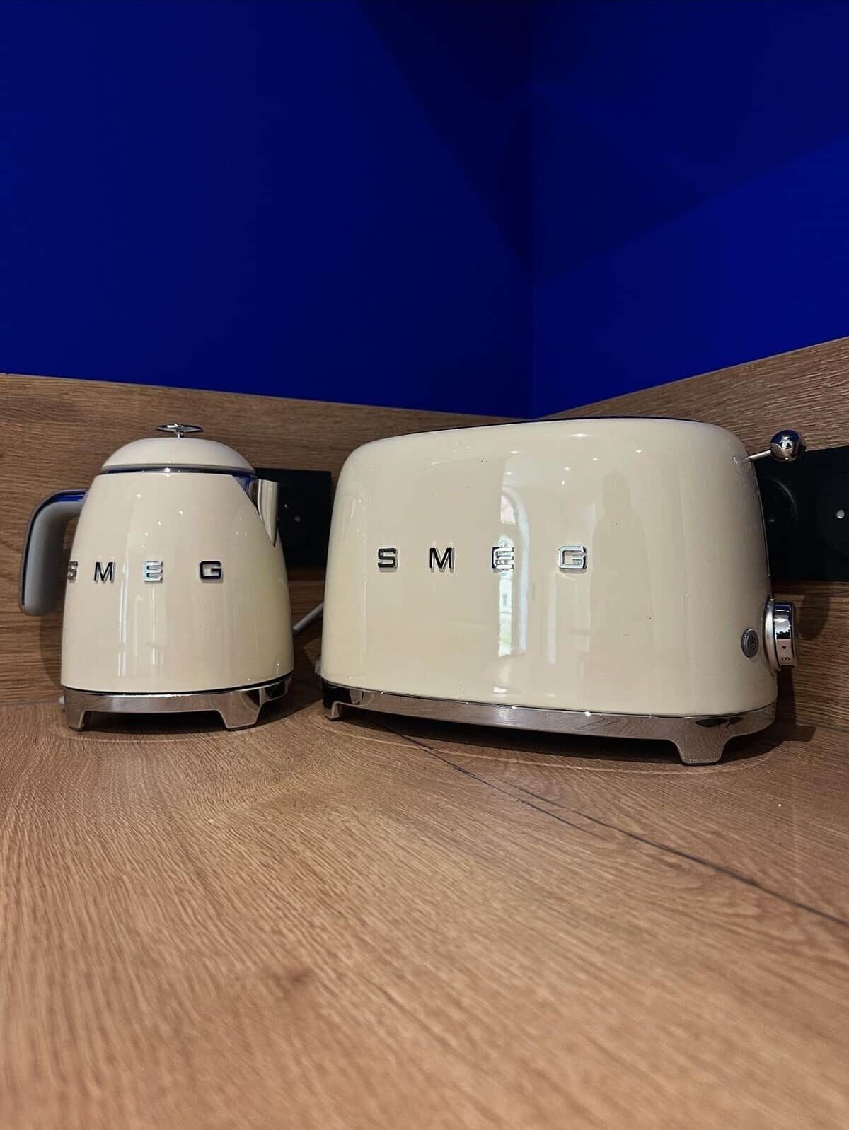 Deux appareils électroménagers blancs, portant la marque « SMEG », sont posés sur une surface en bois.