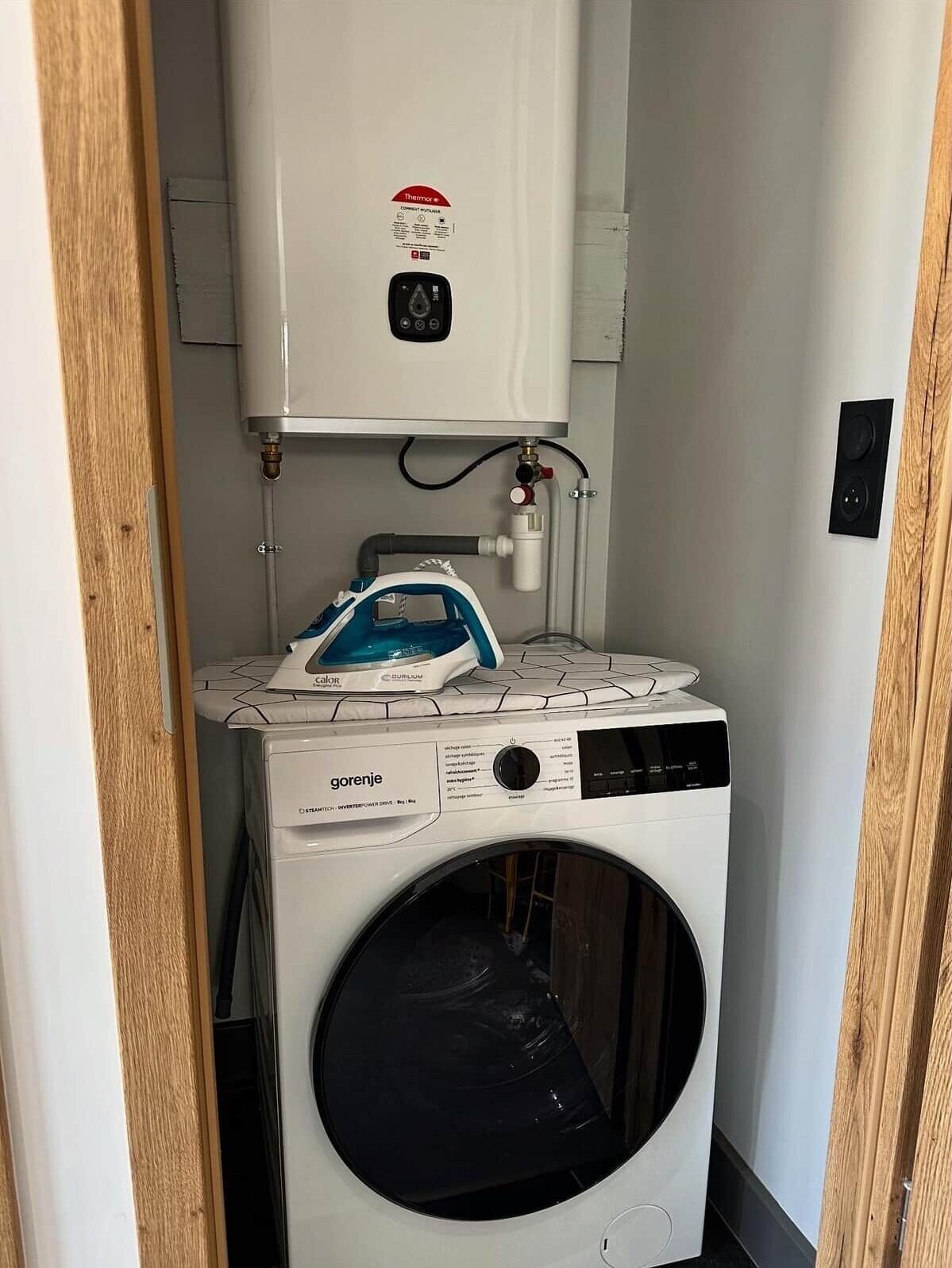 A compact laundry room with a washing machine, a steam iron, and a water heater.