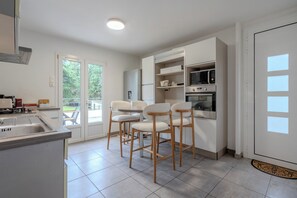 A modern kitchen with a sink, bar stools, a microwave, and an oven.