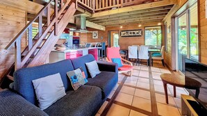 Interior de uma cabana de madeira com escada, sofá, área de jantar e cozinha.