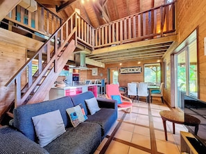 A wooden cabin interior with a staircase, a sofa, a dining area, and a kitchen. - Verger Suspendu - Piscine - Petfriendly (L'Étang-Salé)