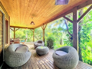 A wooden deck with wicker furniture and a view of lush greenery. - Verger Suspendu - Piscine - Petfriendly (L'Étang-Salé)