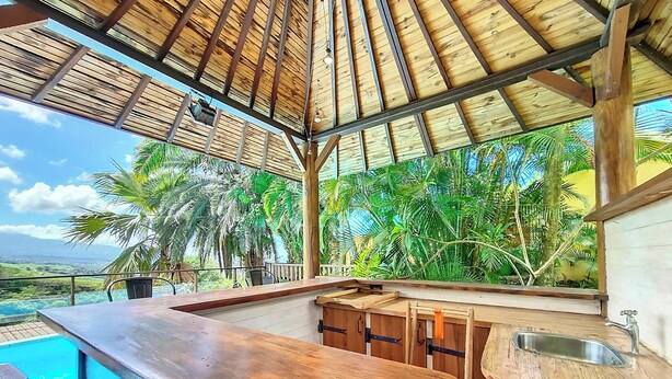Área de bar em madeira com vista para uma piscina e vegetação tropical.