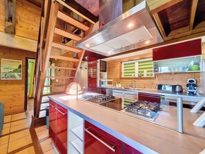 A modern kitchen with a central island, stainless steel appliances, and wooden beams. - Verger Suspendu - Piscine - Petfriendly (L'Étang-Salé)