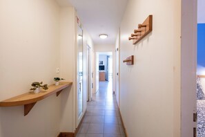A narrow hallway with a wooden shelf holding potted plants, a ceiling light, and a door leading to another room. - Belle Dune - Balcon - Plage (Fort-Mahon-Plage)