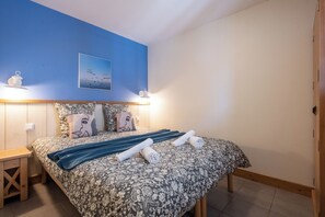 A bedroom with a floral bedspread, two pillows, a blue blanket, and a wall-mounted picture. - Belle Dune - Balcon - Plage (Fort-Mahon-Plage)