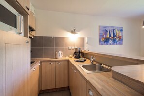 A modern kitchen with wooden cabinets, a stainless steel sink, a coffee maker, and a painting of sailboats on the wall. - Belle Dune - Balcon - Plage (Fort-Mahon-Plage)