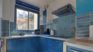 Eine Küche mit blauen Schränken, einer Mikrowelle, einer Kaffeemaschine und einem Fenster mit Blick auf ein Gebäude.
