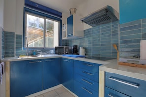 A kitchen with blue cabinets, a microwave, a coffee maker, and a window with a view of a building outside. - Ti paradis - Climatisation - Wifi (Saint-Paul)
