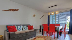 Ein Wohnzimmer mit grauem Sofa, roten Sesseln, einem Esstisch und einem Deckenventilator.
