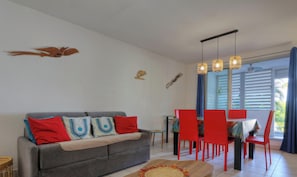 A living room with a grey sofa, red chairs, a dining table, and a ceiling fan. - Ti paradis - Climatisation - Wifi (Saint-Paul)
