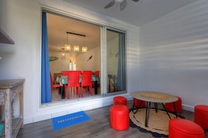 A modern room with a sliding glass door leading to a dining area, a small round table with a rug, and two red stools. - Ti paradis - Climatisation - Wifi (Saint-Paul)