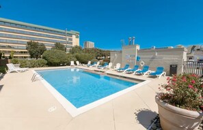 En pool på taket med solstolar och utsikt över en byggnad i bakgrunden.