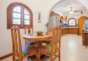 A dining area with a round table and chairs, a kitchen with wooden cabinets, and a water dispenser. - Rooftop Views & Sunsets, Steps to the Malecón (La Paz)