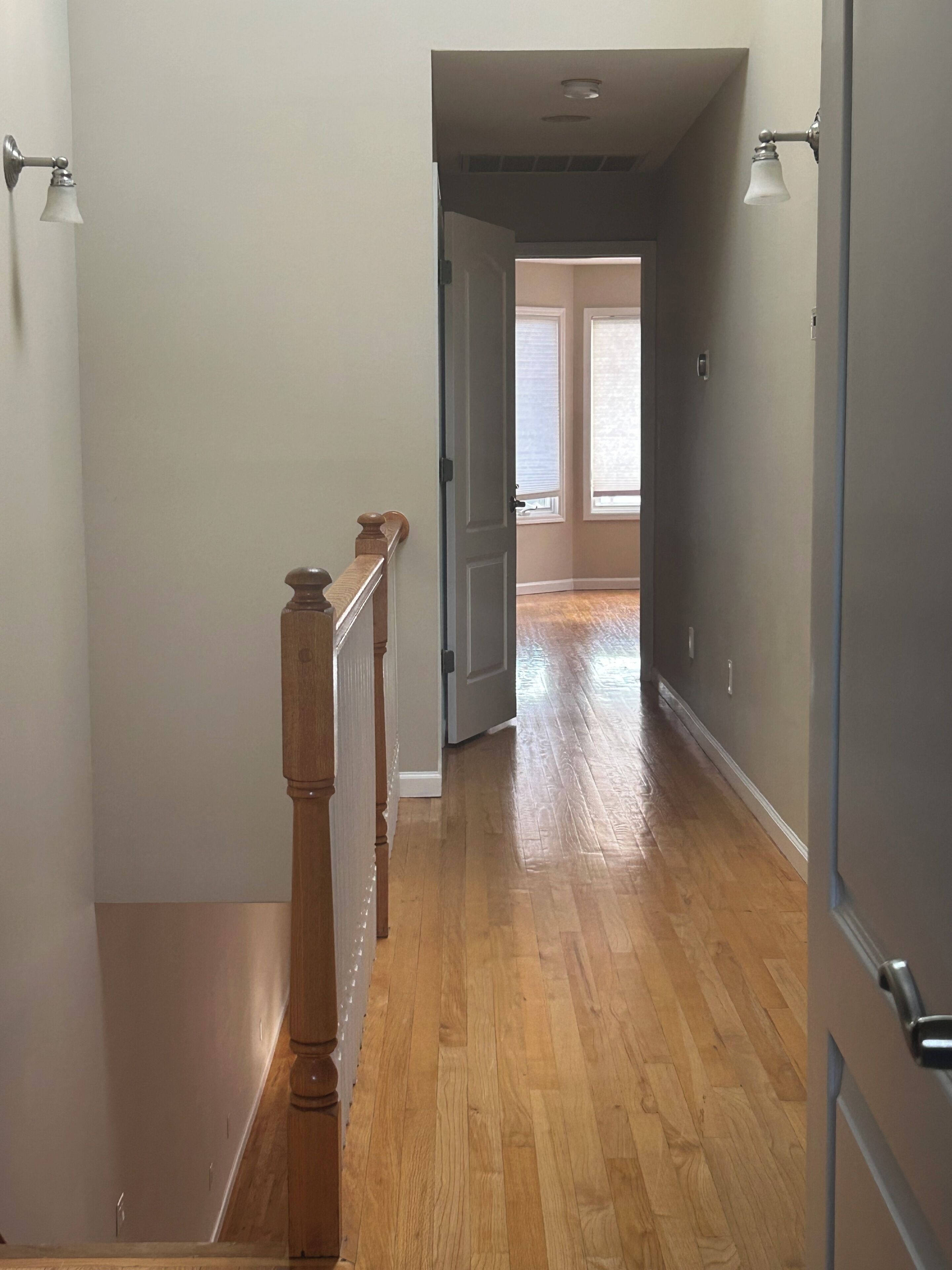 Un passadís amb sòl de fusta, barana de fusta i una porta que dona a una altra habitació.