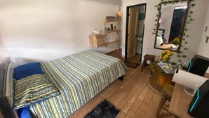 Un dormitorio con cama, escritorio, silla, espejo y una pequeña estantería con objetos personales.