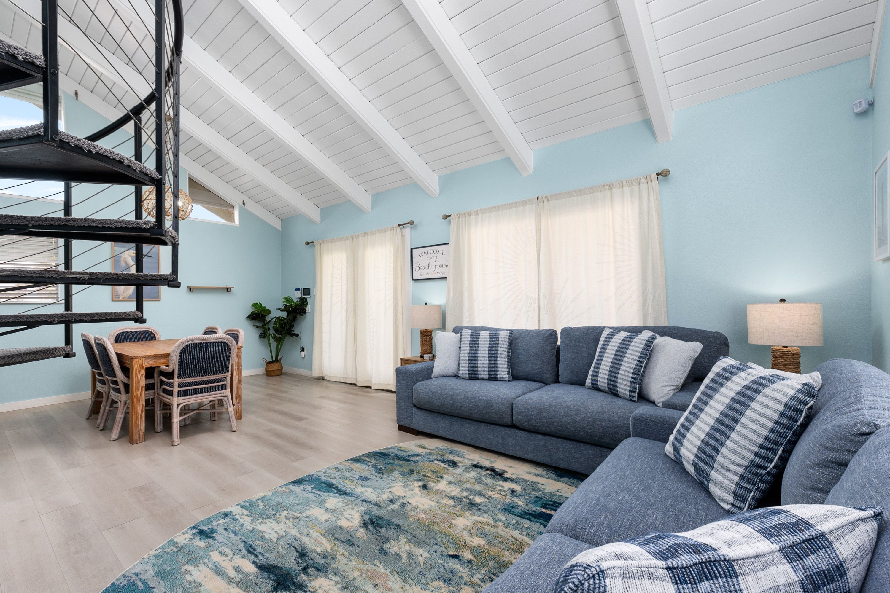 A living room with a sofa, a dining table with chairs, a staircase, and a view of the outside.