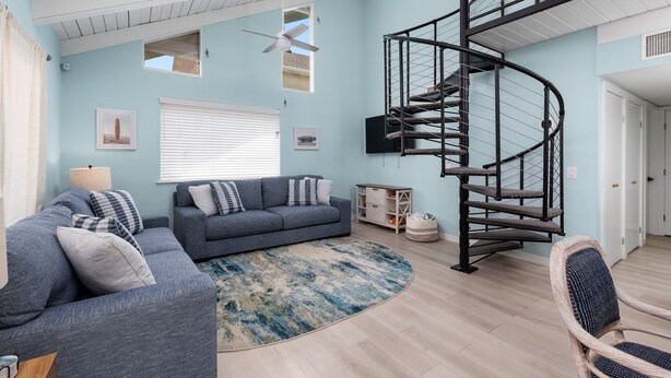 Una sala de estar con una escalera curva, un sofá, un sillón y un ventilador de techo.