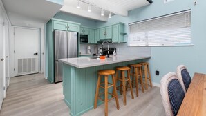 Una cocina moderna con armarios azul verdoso, electrodomésticos de acero inoxidable y taburetes de bar de madera.