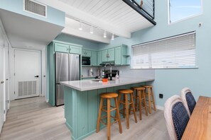A modern kitchen with teal cabinetry, stainless steel appliances, and wooden bar stools. - New remodel w/Pool & feet from the beach! (South Padre Island)