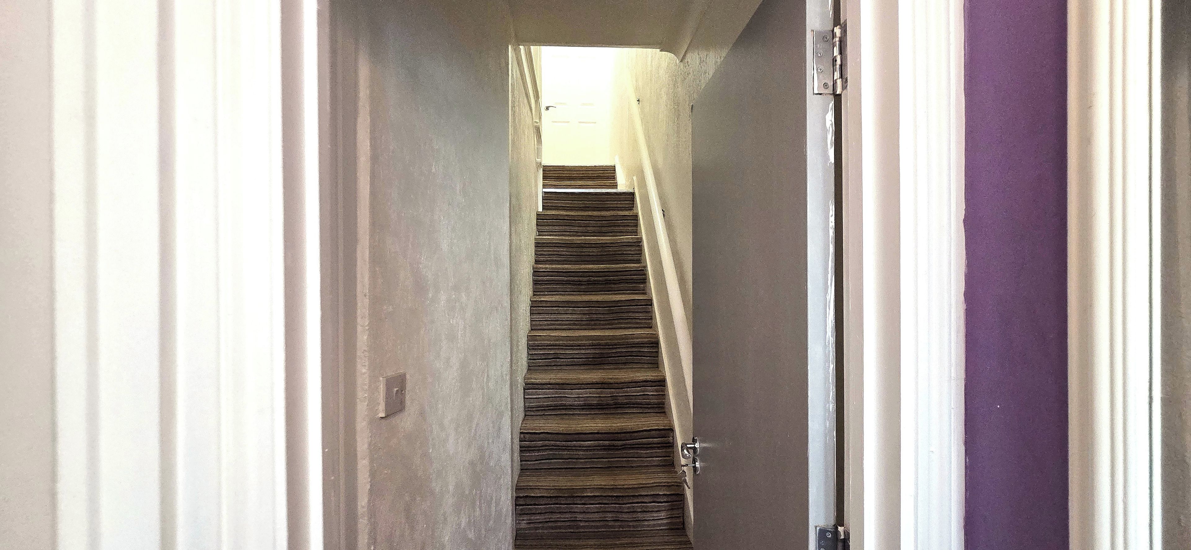 Um corredor estreito com escadas de madeira que levam a um patamar.