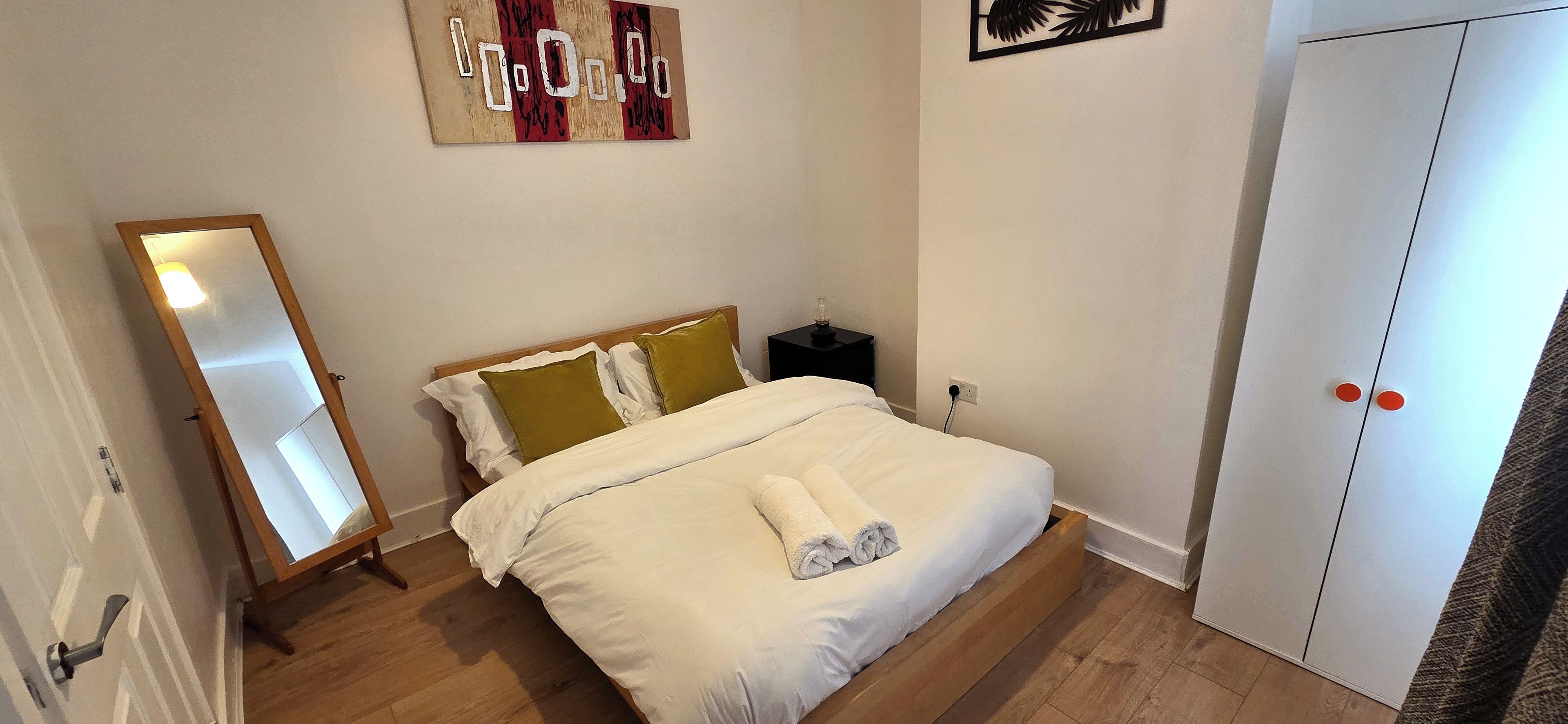 Quarto com cama, mesa de cabeceira, guarda-roupa e espelho.