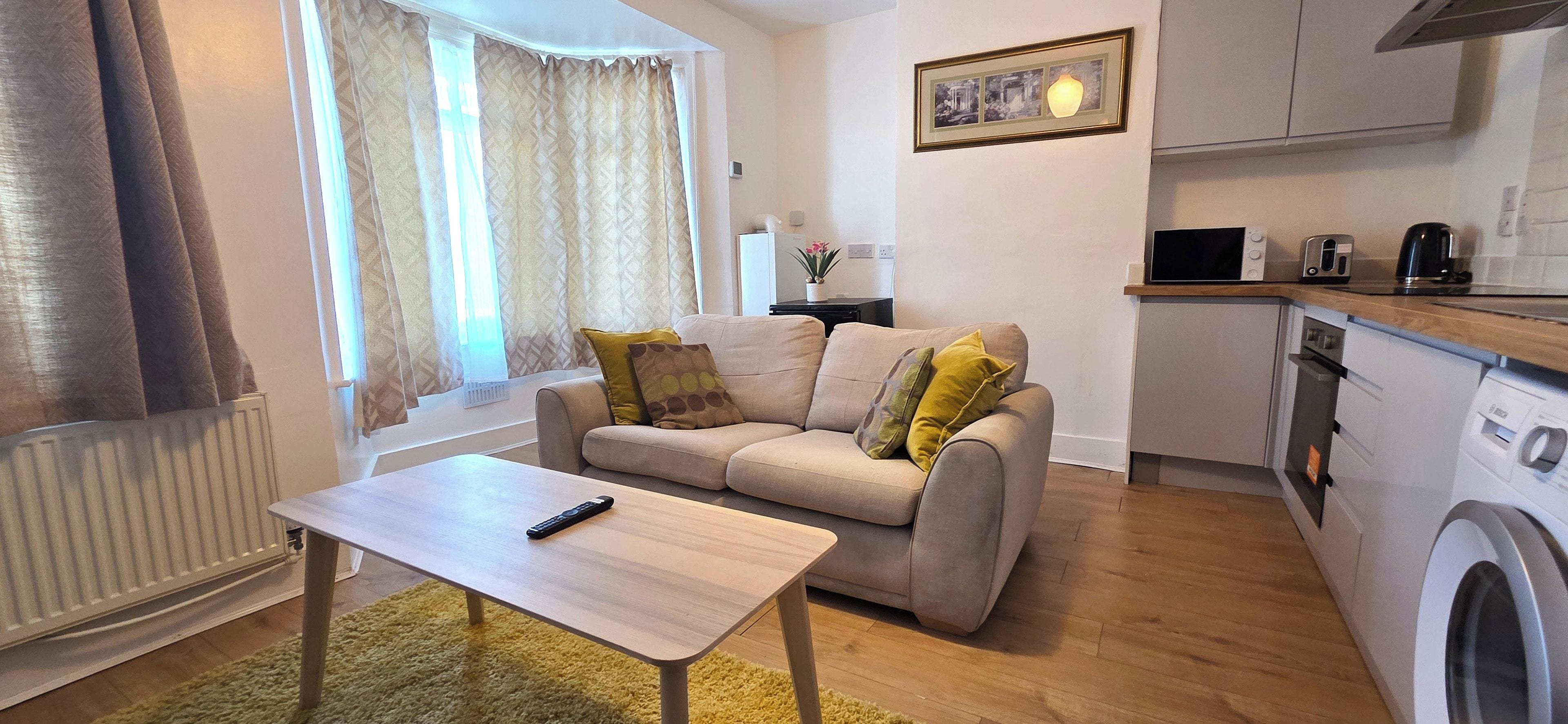 Un espace de vie compact comprenant un canapé, une petite table, un lave-linge et une kitchenette.
