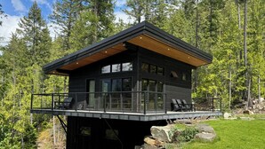 A modern cabin with a deck, large windows, and a forest backdrop. - Modern-Japanese Inspired - Indoor/Outdoor Luxury Rental (Riondel)