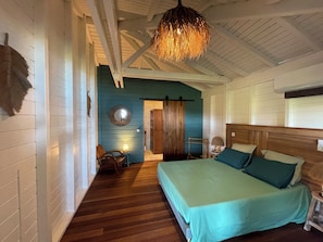 Ein Schlafzimmer mit Bett, einem Holz-Kopfteil, einer Hängeleuchte, einem Spiegel und einer Tür zu einem anderen Raum.