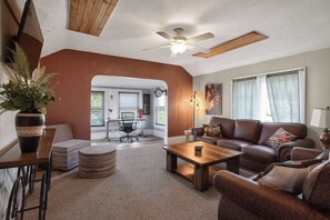 Ein Wohnzimmer mit braunem Sofa, einem Couchtisch, einem Deckenventilator und Blick ins Freie.