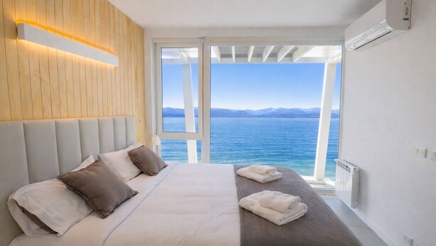 Ein Schlafzimmer mit Bett, Kissen, einem Nachttisch mit Handtüchern, Blick auf das Meer und einer Klimaanlage.