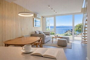 A modern living room with a wooden floor, a dining table with chairs, a sofa, a coffee table, and a book on the table. - Signature Lake View Luxury Residences B04 (BARILOCHE - SAN CARLOS DE BARILOCHE)