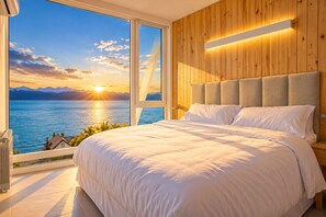 A bedroom with a large bed, a wooden headboard, and a view of a lake and mountains through a large window. - Signature Lake View Luxury Residences Unit H25 (BARILOCHE - SAN CARLOS DE BARILOCHE)