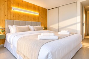 A modern bedroom with a wooden panel wall, a large bed with white bedding, a bedside table with a lamp, and a sliding door closet. - Signature Lake View Luxury Residences Unit H25 (BARILOCHE - SAN CARLOS DE BARILOCHE)