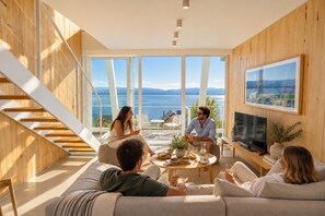 A modern living room with a large TV, a sofa, a coffee table, and a staircase leading to a balcony with a view of the sea. - Signature Lake View Luxury Residences Unit H25 (BARILOCHE - SAN CARLOS DE BARILOCHE)