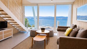 Un soggiorno moderno con TV, divano e zona pranzo, affacciato su una vista panoramica dell'oceano.