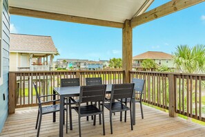 Een overdekt terras buiten met een tafel en stoelen, houten leuningen en uitzicht op omliggende huizen.