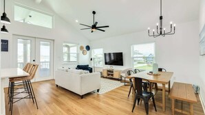 Un'ampia zona giorno con tavolo da pranzo, divano e TV, caratterizzata da luce naturale e ventilatore a soffitto.