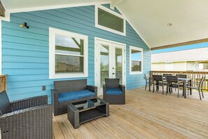 Een overdekt terras met een blauwe buitenmuur, rieten meubels en een houten tafel.