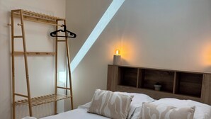 Una camera da letto con una scala in legno, una lampada a sospensione, un letto con cuscini decorati e una pianta sul comodino.