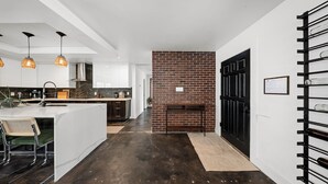 Een moderne keuken met hanglampen, een bakstenen muur en een zwarte deur.