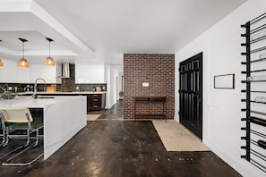 Une cuisine moderne avec des luminaires suspendus, un mur en briques et une porte noire.