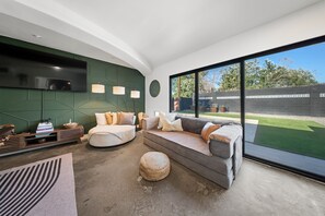 Un salon moderne doté d’un grand téléviseur, de sièges confortables et offrant une vue sur l’extérieur.