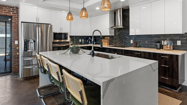 Een moderne keuken met een centraal eiland, roestvrijstalen apparatuur en hangende lampen.