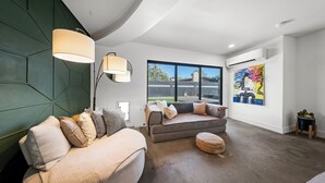 Een moderne woonkamer met een hoekbank, een rond hocker en een groot raam met uitzicht op de omgeving.