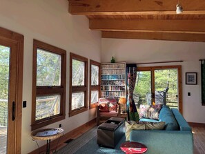 A cozy room with large windows, a bookshelf, a sofa, and a small table. - Burns No.8 - Cottage on the Bay (Kewadin)